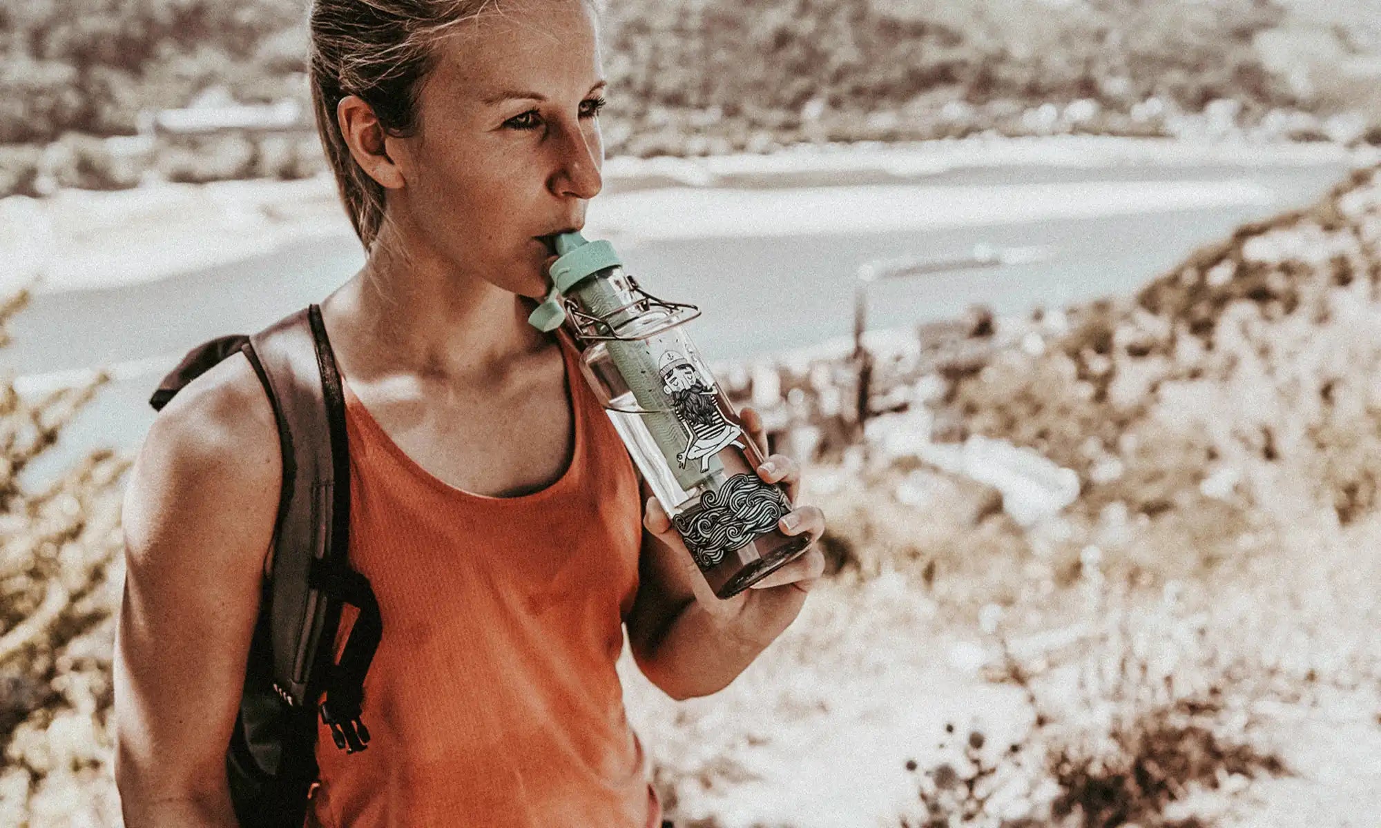 Frau beim Wandern mit Glastrinkflasche und integriertem Wasserfilter trinkt