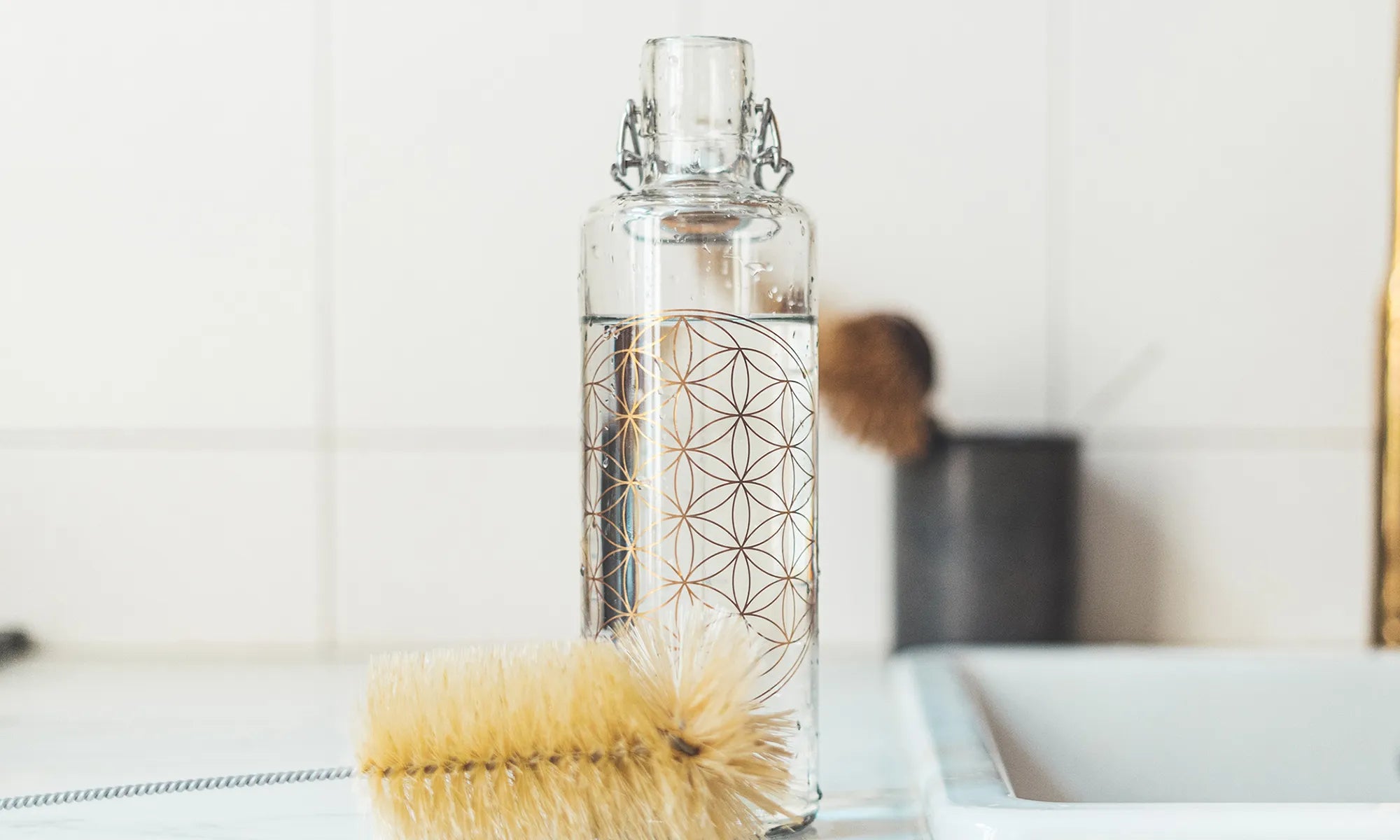 Trinkflasche aus Glas mit Blume des Lebens neben Spülbecken