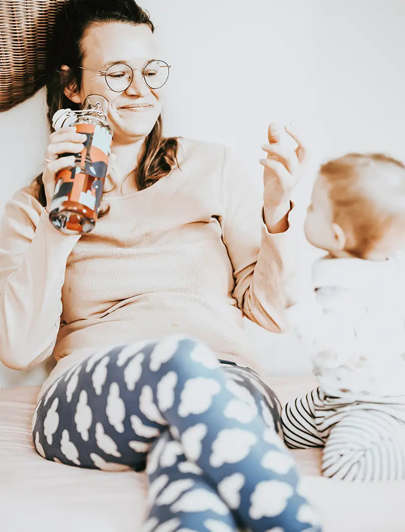 Frau mit Baby hält Trinkflasche in der Hand