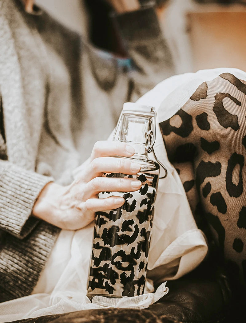 Frau mit Trinkflasche und Leopardenmuster auf COuch