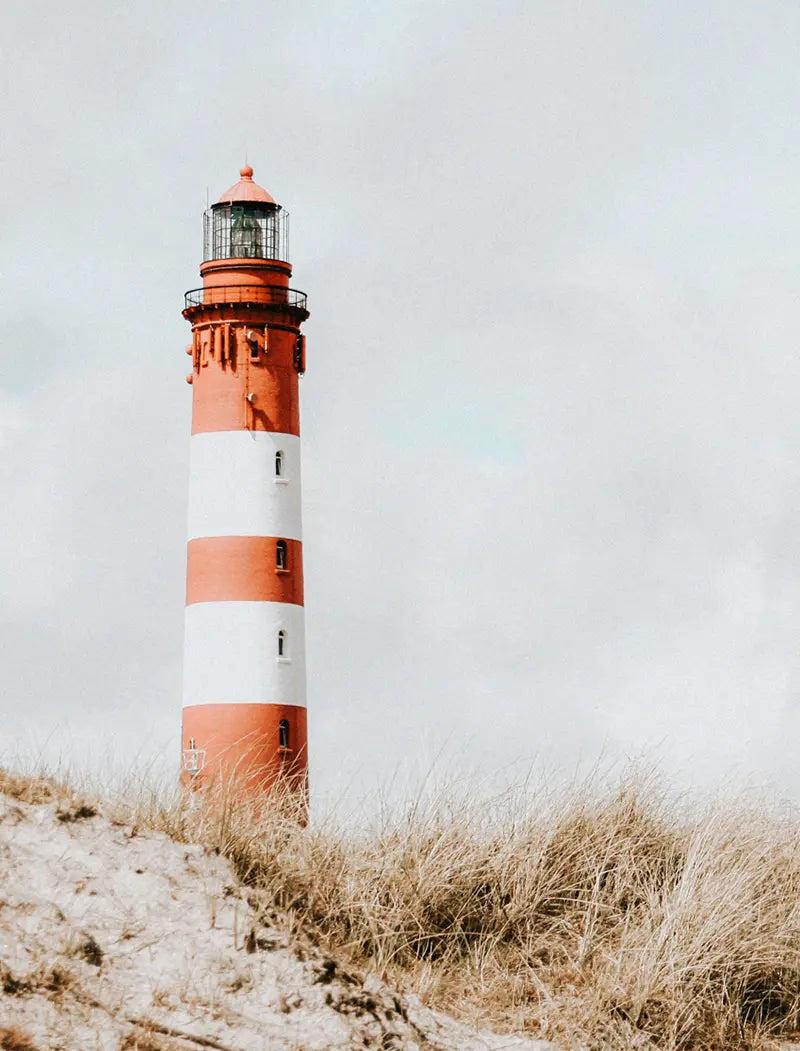 Leuchtturm mit roten Streifen hinter einer Düne