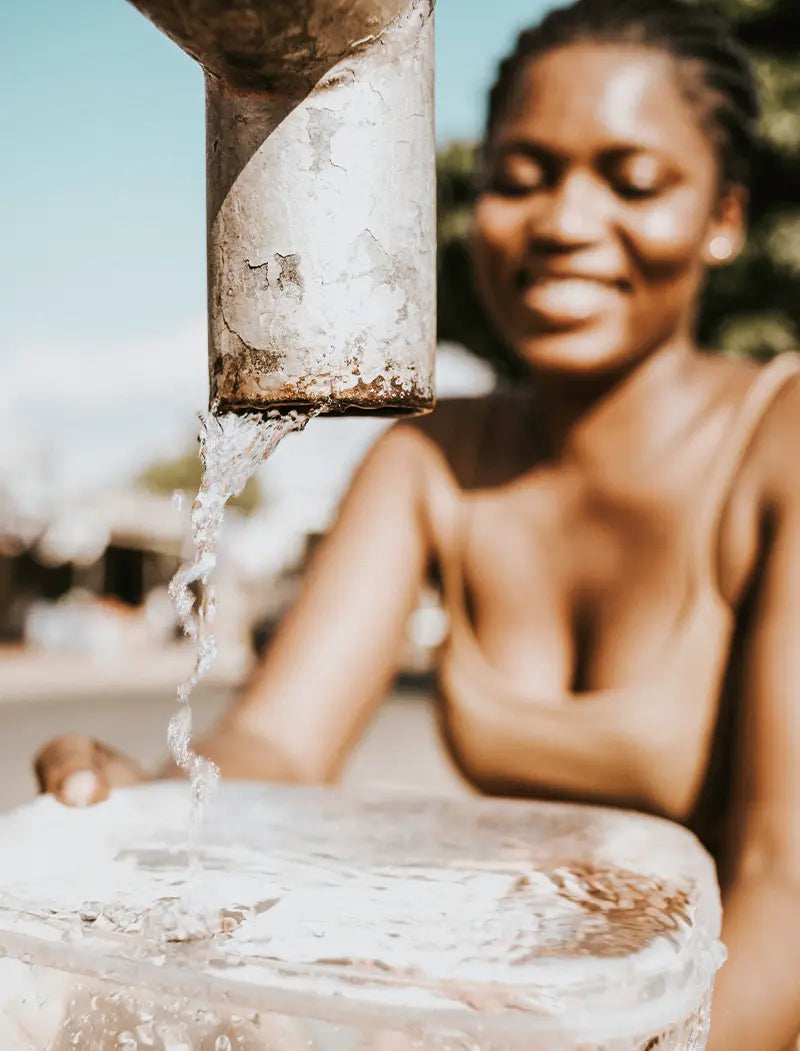 schwarze Frau zapft Wasser an öffentlichem Brunnen