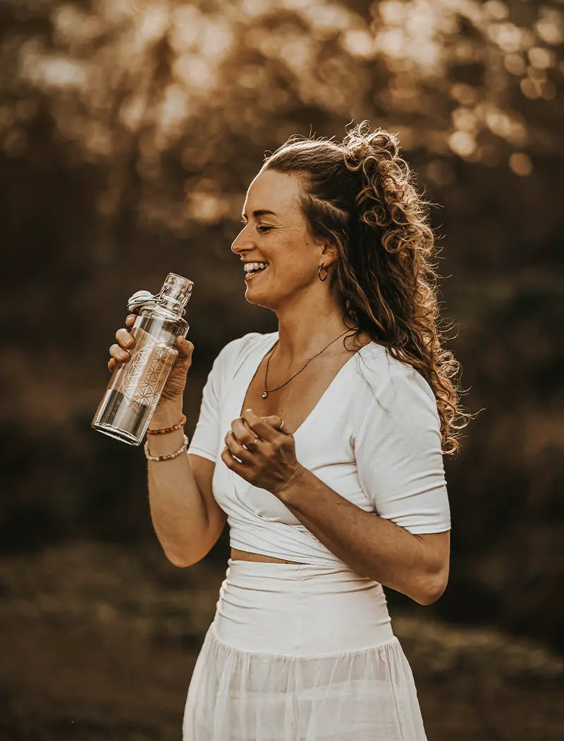 Frau in der Natur mit Trinkflasche in der Hand mit Blume des Lebens Motiv